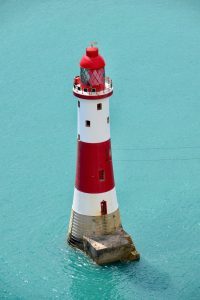 Faro blanco y rojo sobre plataforma en medio del mar para dar luz y motivar